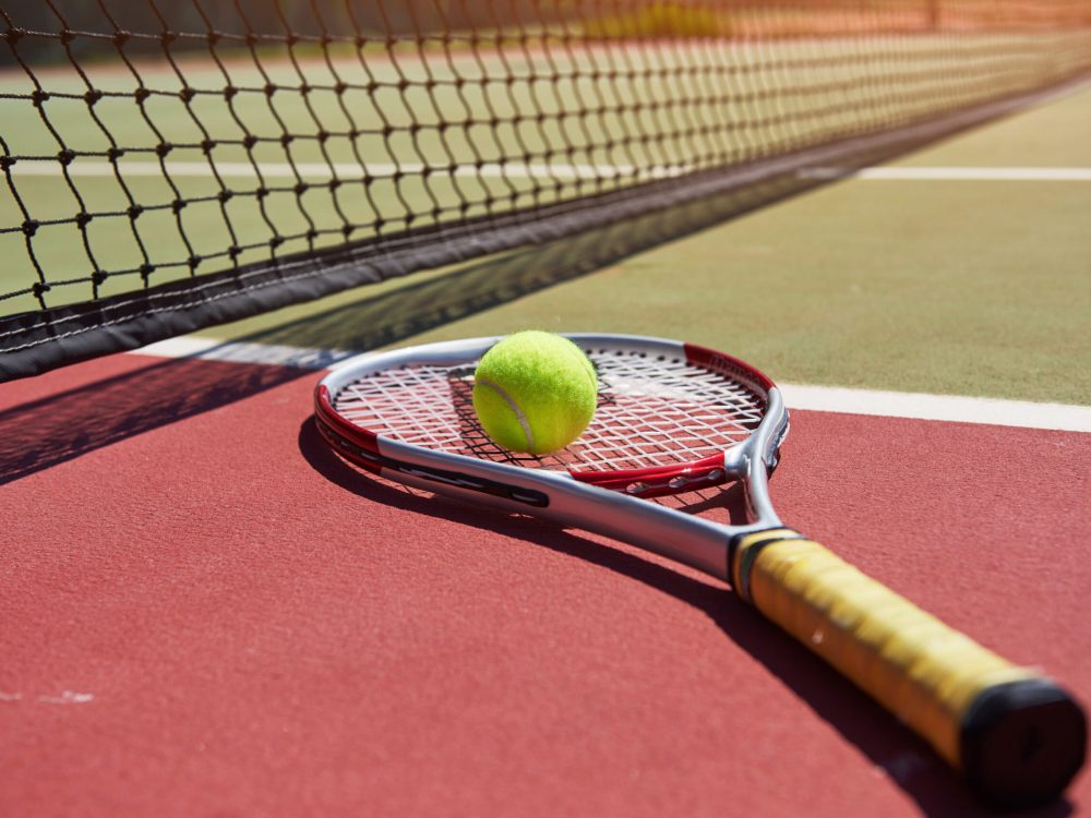 A tennis racket and new tennis ball on a freshly painted tennis court.