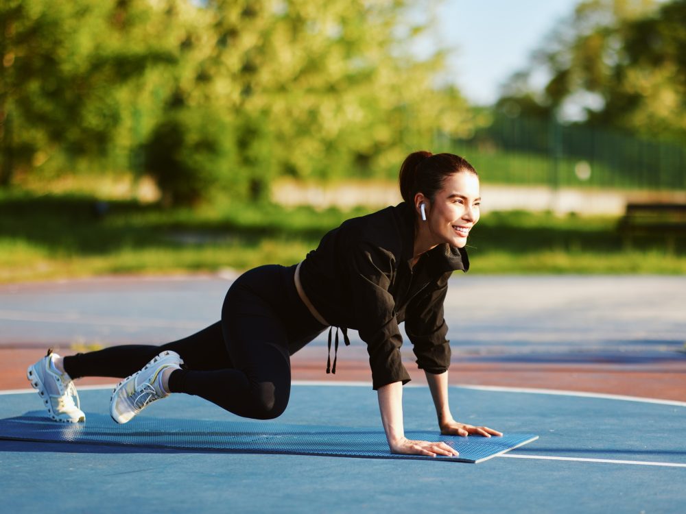 Young sportswoman doing mountain climber exercise on fitness mat outdoors